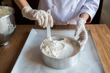 Female chef cook in rubber gloves preparing vanilla cake-mix dough in form for baking cake. Young...