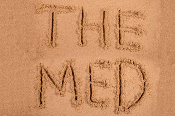 The Med written in soft wet sand on a beach