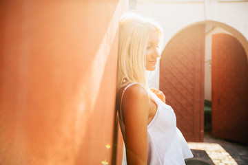 Bright atmospheric photo of gorgeous blond woman i posing over orange wall with beautiful sun rays at the summer time in the morning. Close up portrait