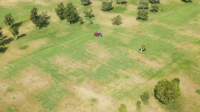 Vista aerea di un gruppo di giardinieri che lavora e cura l'erba. Una macchina, chiamata tosaerba, tosa il prato. Il campo da lavorare è grande e richiede molte cure e attenzioni.