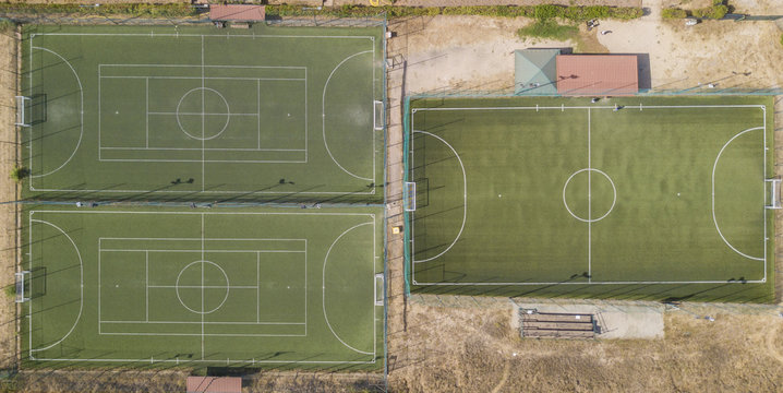 Vista aerea perpendicolare di tre campi di calcio a 5 in erba sintentica. A bordo campo panchine e ombrelli. I campi sono vuoti perch&egrave; &egrave; estate e fa caldo.