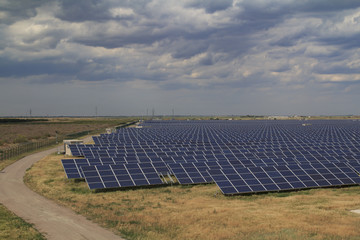 Solar panels array of a power station in the field of Ukraine with a heavy sky and dry grass