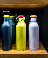 Stainless steel vacuum water bottle with twist off lid for cold beverages on wooden shelf.