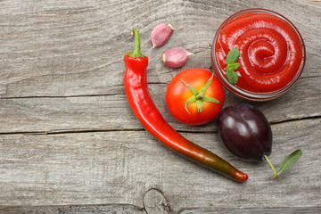 raw plum, tomato and ketchup on wooden table. top view