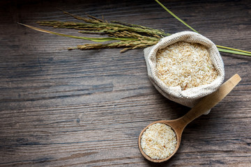 Rice in a wooden spoon and rice sack on a wooden table 