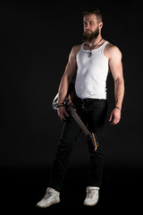 Fototapeta premium KIEV, UKRAINE - May 03, 2017. A charismatic and stylish man with a beard holds an electric guitar in his hand on a black isolated background. Vertical frame