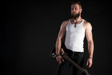 Fototapeta na wymiar KIEV, UKRAINE - May 03, 2017. A charismatic and stylish man with a beard holds an electric guitar in his hand on a black isolated background. Horizontal frame