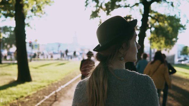 Back view of young beautiful woman walking in the park in evening. Female in hat enjoying the scenic sunset.