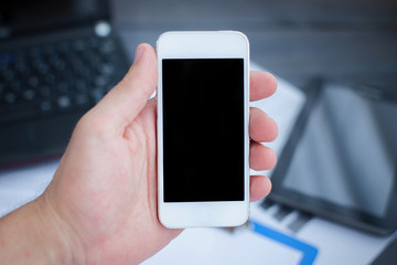 Business and technology background. Hand holding empty copy space screen of mobile phone with tablet and laptop in the background.