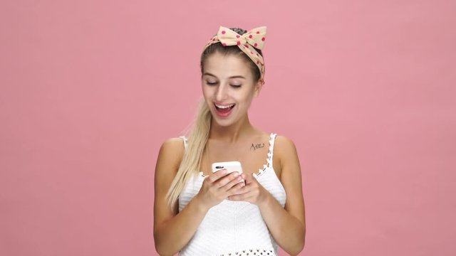 Young smiling caucasian lady chatting with friends by phone over pink background