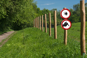 Two round red warning signs on a fence post in front of a green meadow.