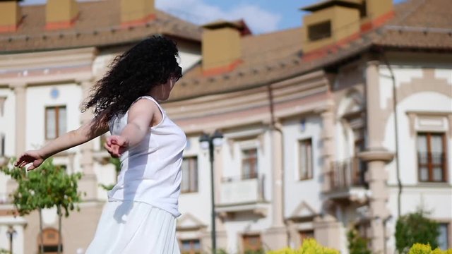 Happy woman dancing outdoors, slow motion. Happy girl enjoying life and dancing in dance laughing. Young beautiful brunette in white dress is dancing outside, smiling, relaxes and enjoys life.