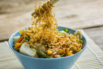 Chopsticks while eating Fried instant noodles in blue cup.
