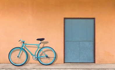 The green door and the orange wall have a parked bicycle against the wall.