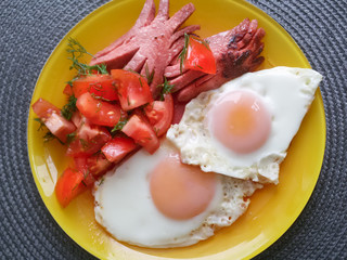 Scrambled eggs,fried sausages and sliced tomatoes on a yellow plate.