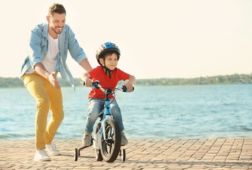 Young man teaching his son to ride bicycle outdoors near river