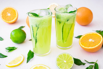 Fresh transparent refreshing drink with cucumber, limes and orange on white wooden table