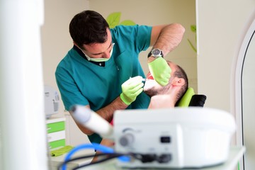 Young handsome man sitting on dental chair while his young male dentist fixes his teeths
