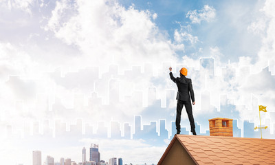 Man architect draw silhouette of modern city on blue sky. Mixed media
