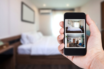 Hand holding smartphone view looking in house on blurred house background with Home security CCTV system concept.