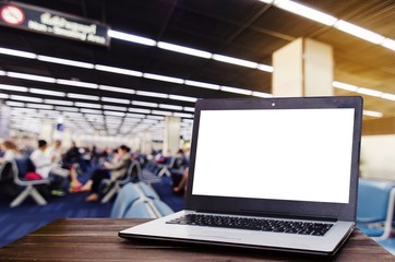Laptop computer with white blank screen on wooden desk with blurred view of passenger waiting in the airport terminal, copy space, working outside office, online social media, searching data concept