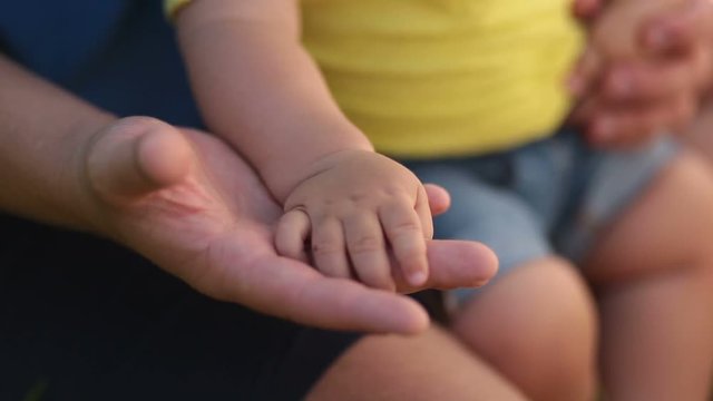 Father holding hand of infant son in his palm