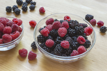 Raspberries and blackberries in a glass jar on a wooden table.