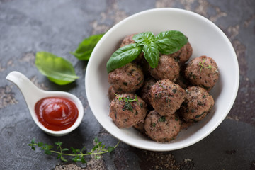 Oven-baked meatballs in a white bowl with sauce, studio shot on a brown stone surface