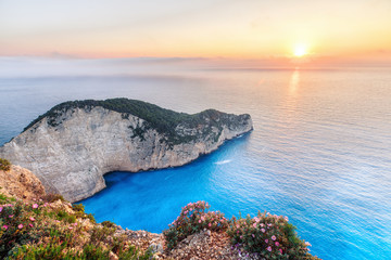 Obrazy na Plexi  Zachód słońca dekoracje z tarczą słońca spadającą za Morze Jońskie na plaży Navagio z widokiem na wrak statku, Zakynthos - Zante island w Grecji. Bardzo popularny i znany cel podróży na letnie wakacje.