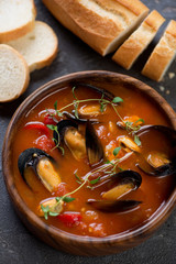 Tomato soup with mussels served in a wooden bowl, close-up, vertical shot, elevated view