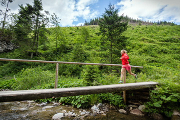 Fototapeta na wymiar Young woman running on bridge in mountains on summer day