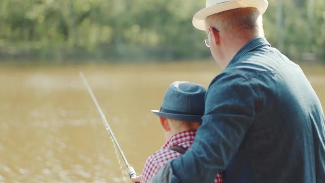 Close up backshot of little boy and his granfather in straw hats fishing together