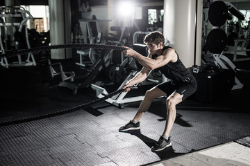 Fototapeta na wymiar Fitness man working out with battle ropes at gym. Battle ropes fitness man at gym workout exercise fitted body. Fitness man training with battle rope in fitness club. Training with battle rope