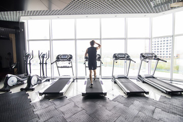 Running fast. Back view of young man in sportswear running on treadmill at gym