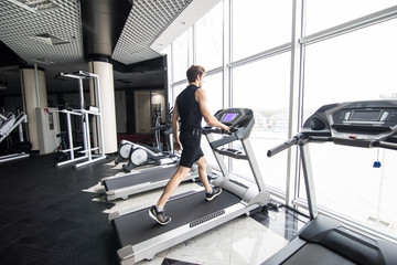 Running fast. Side view of young man in sportswear running on treadmill at gym