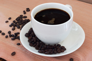 Hot coffee in white cup and coffee beans on the table
