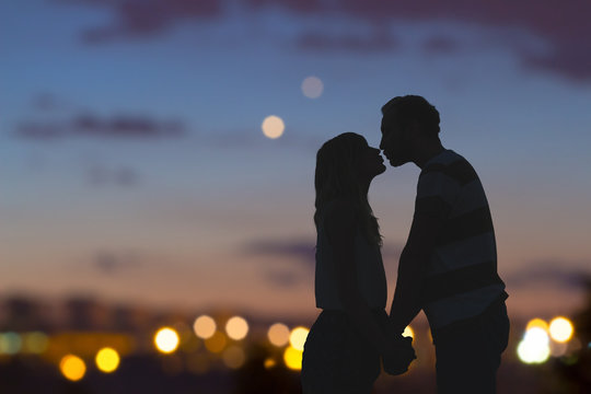 Silhouettes of a young couple kissing with city panorama in the background.