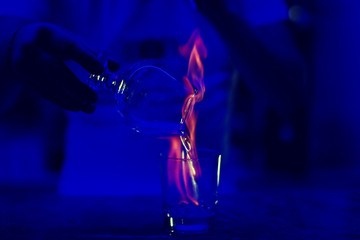 Barman's hands in bar interior making alcohol flaming cocktail. Professional bartender at work in bar mixing drink with burning fire. Deep