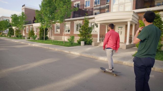Back view of three friends riding skateboards in summer day. Young people in casual outfit skating along the street. Extreme sports enthusiasts spending time outdoors demonstrating healthy lifestyle.