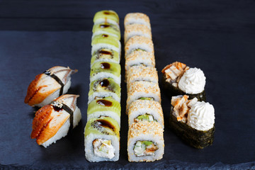 Various sushi set of nigiri, gunkan and maki rolls on black stone background, top view, horizontal border. Japanese and Asian food.
