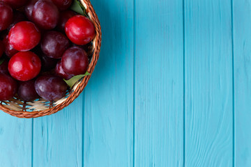 Plums in basket on light blue table. Freshness, harvest, fruits concept. Free space for advertisement or text