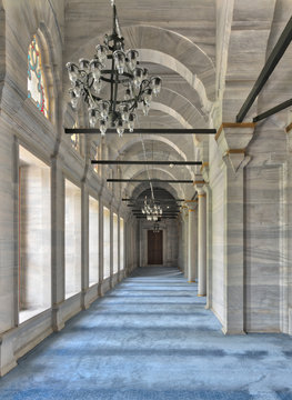 Passage in Nuruosmaniye Mosque, a public Ottoman Baroque style mosque, with columns, arches and floor covered with blue carpet lighted by side windows located in Shemberlitash, Fatih, Istanbul, Turkey