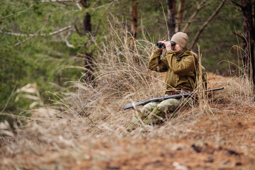female hunter with binoculars ready to hunt, holding gun and walking in forest.