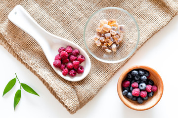Making summer preserve. Raspberry, blueberry and sugar on white and canvas background top view
