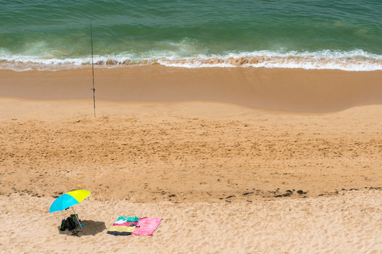 Summer view from above of sun parasols and a fishing rod on a sunny beach in Portugal.