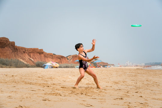 Cute youg girl in swimsuit standing on a beach by the sea throwing a disc.