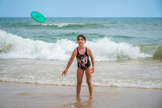 Cute youg girl in swimsuit standing in water with waves throwing a disc.
