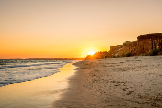 Beautiful colorful sunset in Algarve Portugal. Peaceful beach water and cliffs.