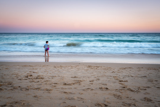 Long exposure image of young girl standing on a beach with waves, sunset in Portugal.