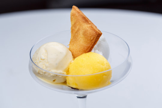 Two different scoops of ice cream with cake and passion fruit in a glass.